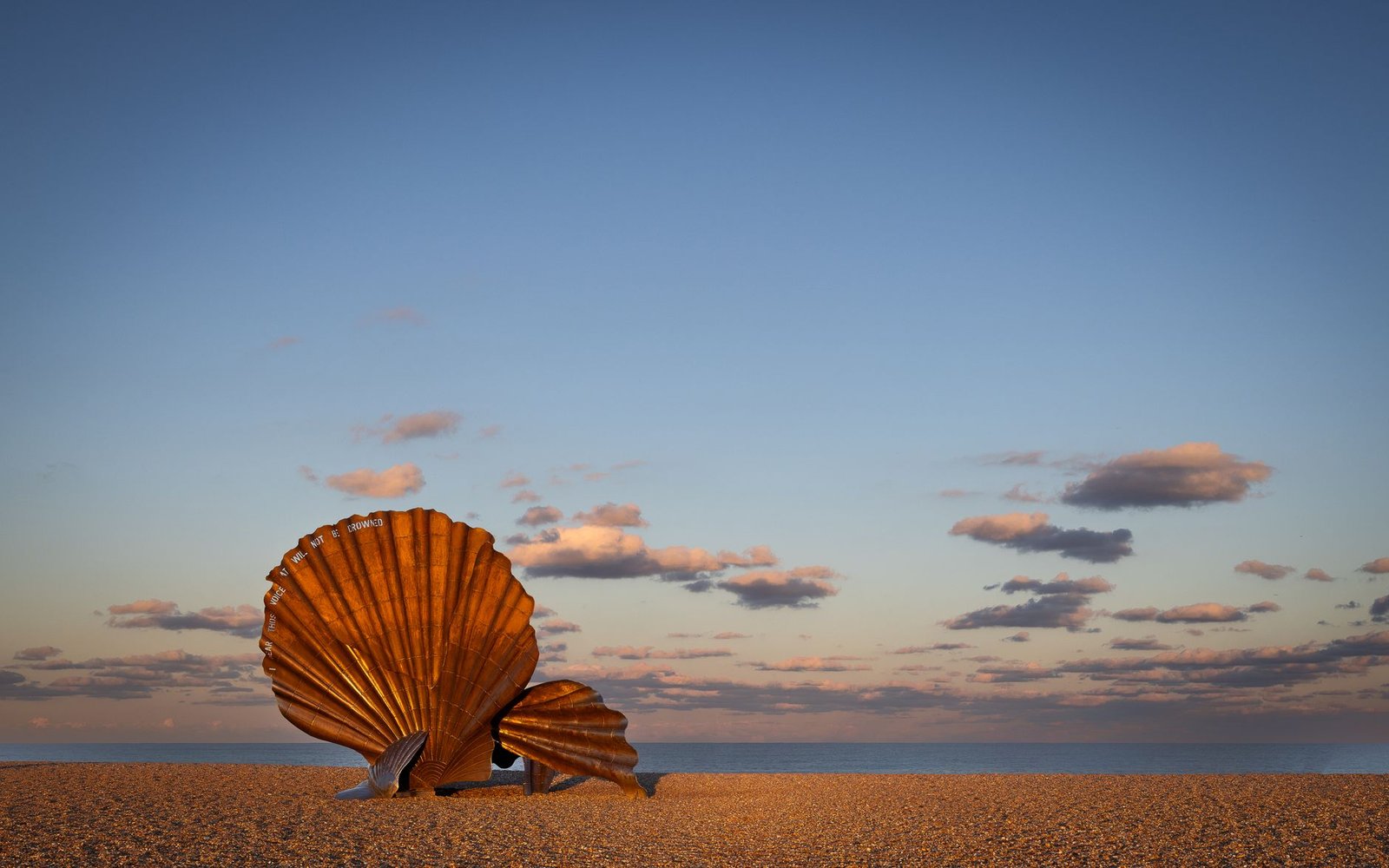 Iconic Scallop sculpture on Aldeburgh beach under a serene sky at sunset.