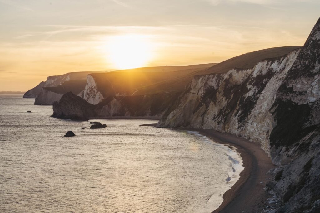 Experience the scenic beauty of a sunset over dramatic cliffs and calm sea.
