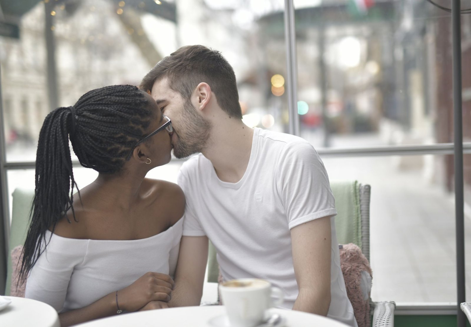 A couple sharing a romantic kiss at a cozy café, highlighting love and diversity.