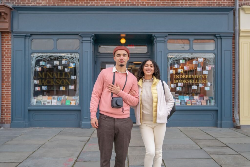Cheerful young ethnic couple with photo camera smiling and looking at camera near urban building