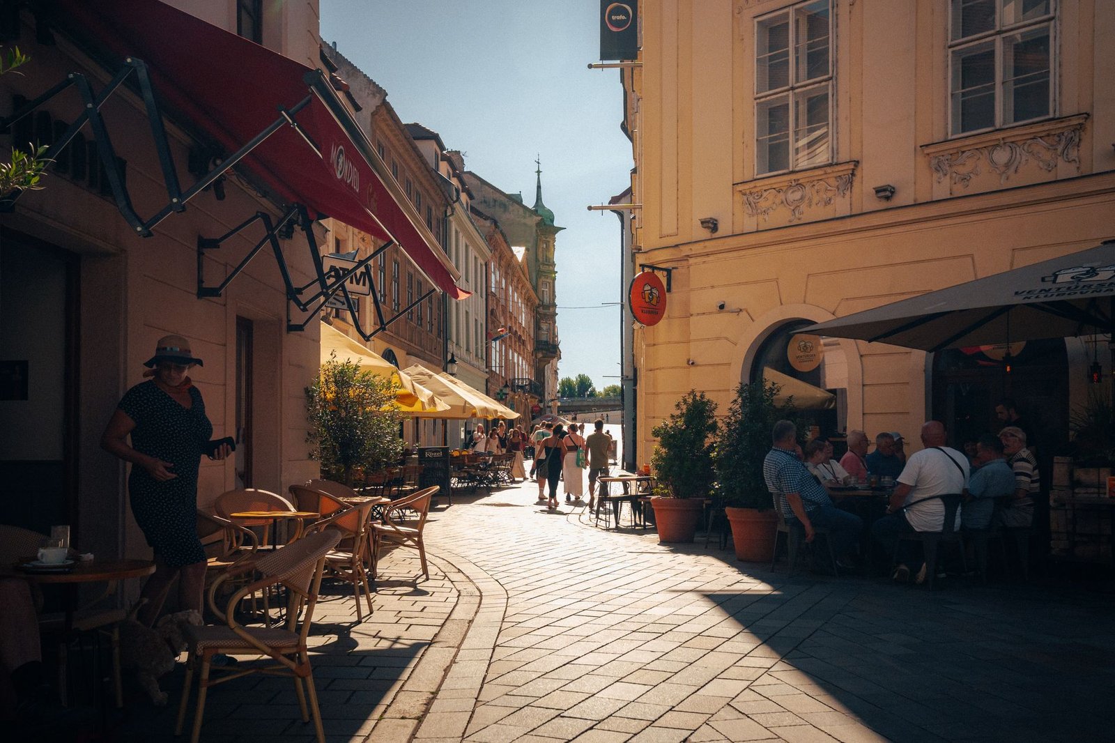 Busy street in Bratislava's Old Town with people enjoying cafes and architecture in the summer sun.