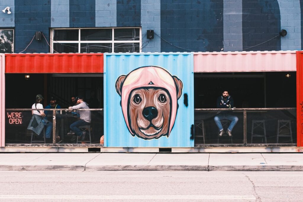 A lively outdoor cafe in Denver with colorful shipping container design and vibrant street art mural of a dog.