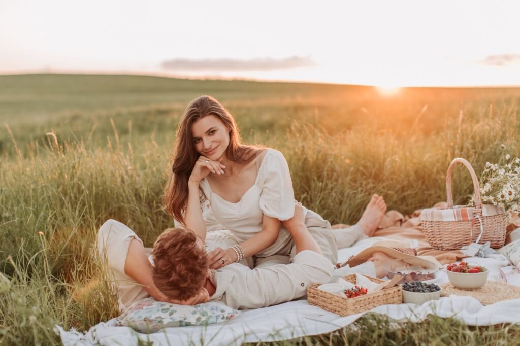 A couple enjoying a romantic picnic in a scenic grass field during sunset.