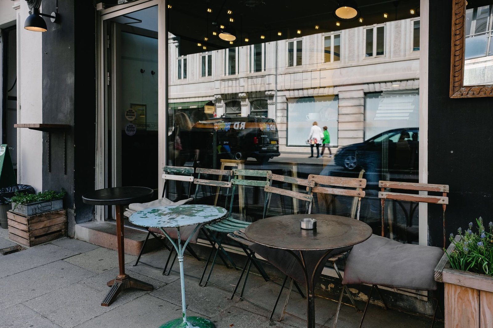 Cozy outdoor café with vintage seating and street reflections in Copenhagen.
