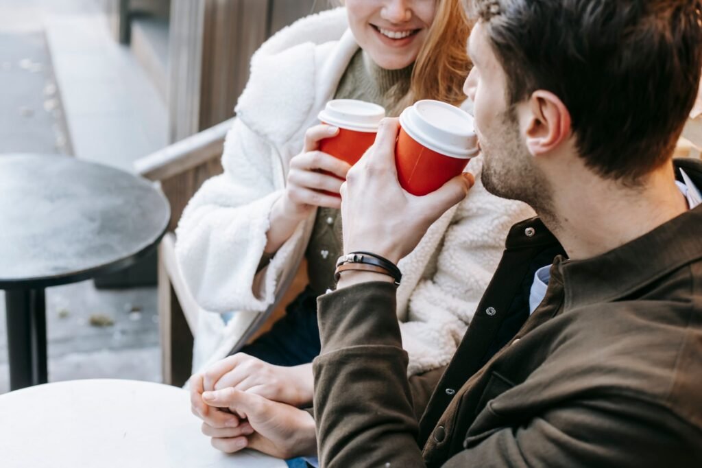 Crop positive young lady and guy wearing casual outfit communicating while sitting on bench and holding hands during date wit