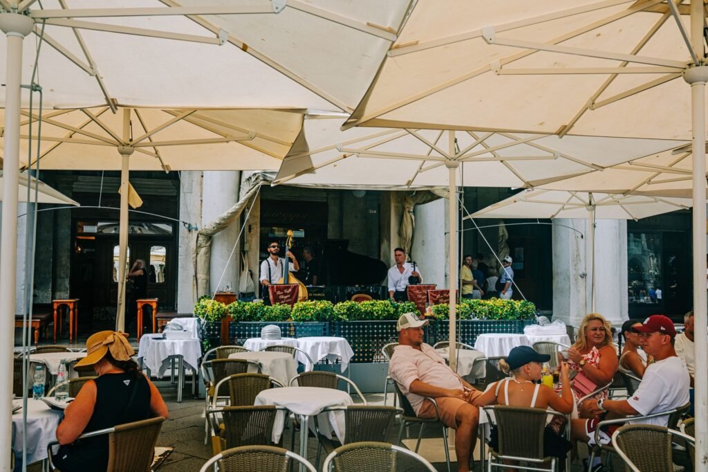 Lively outdoor cafe scene featuring diners and musicians under umbrellas on a warm summer day.