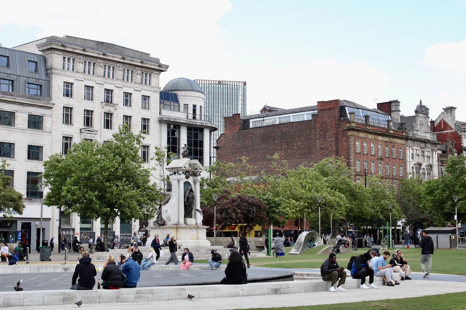 Bustling city square featuring a historic statue surrounded by diverse people.