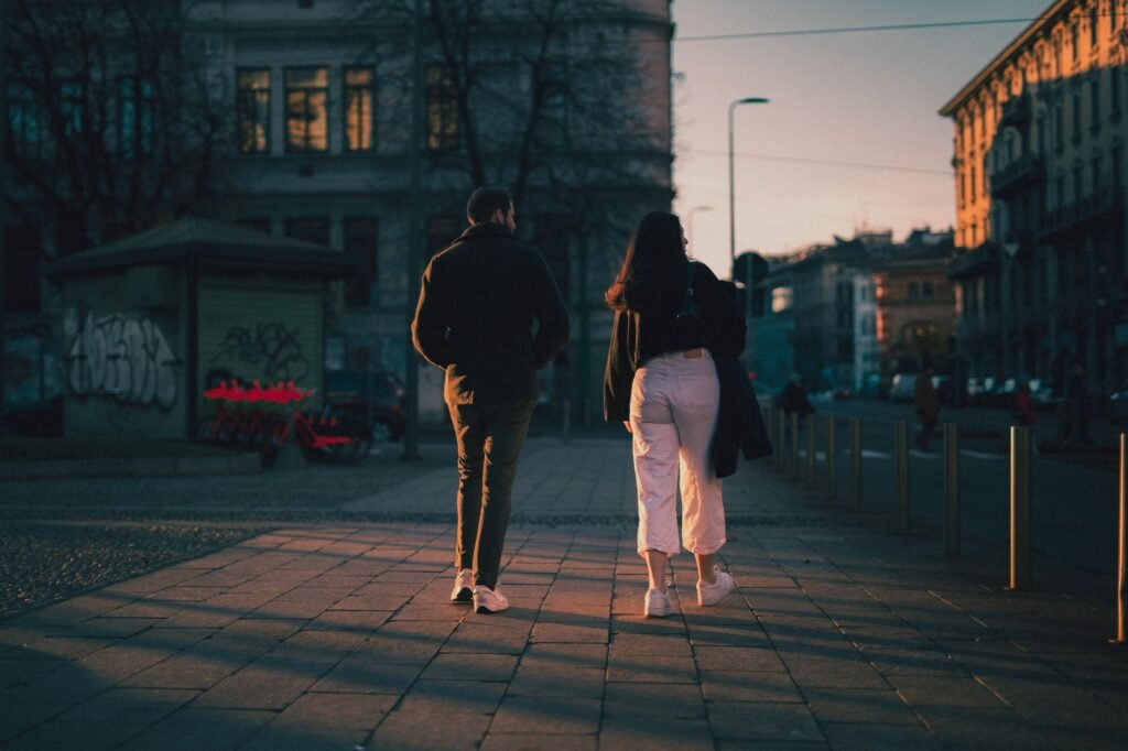 A man and woman walking down a city street during sunset, capturing urban life.