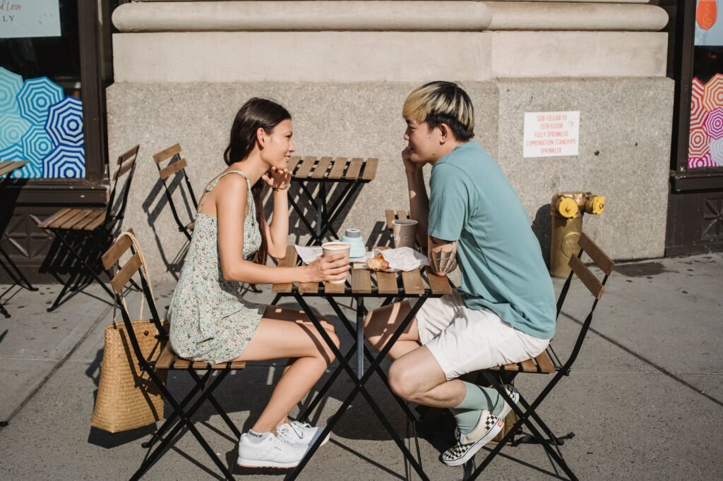 Side view of young multiracial couple looking at each other and drinking coffee on street on sunny day