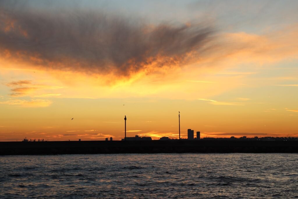 A breathtaking sunset over the sea with a city skyline and vivid clouds.
