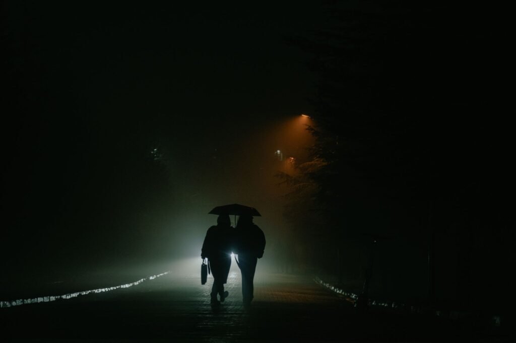Moody silhouette of a couple with umbrella strolling under street lights in a foggy street.