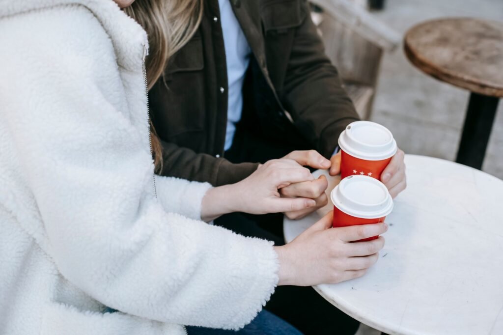 Unrecognizable couple in casual clothes having hot beverage in small cafe holding hands together