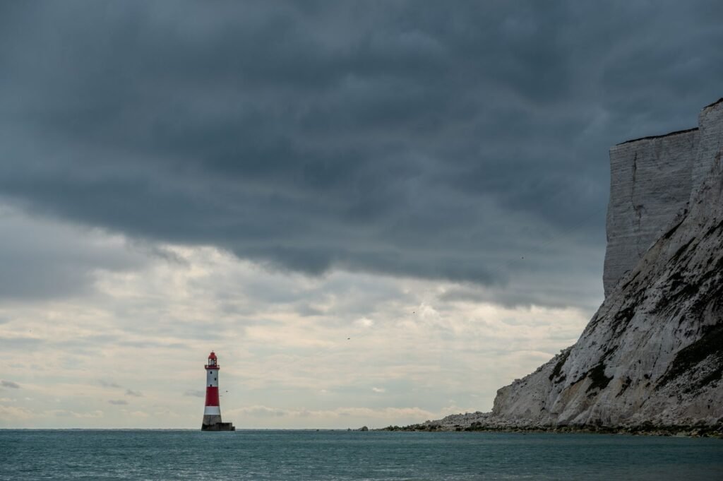 Dramatic view of Beachy Head Lighthouse against cloudy sky, near white cliffs in England.