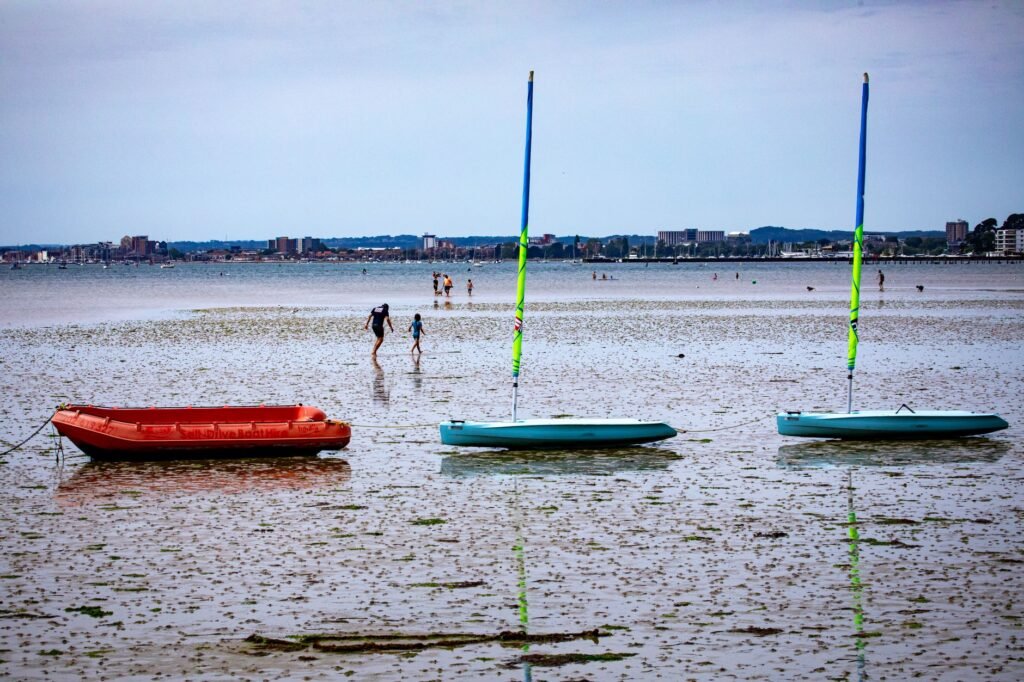 A vibrant beach view in Poole, England featuring moored boats and distant people enjoying a coastal day.