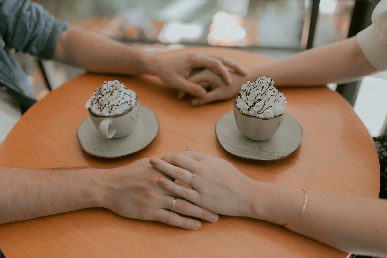 Couple holding hands over hot chocolate at a cozy cafe setting.