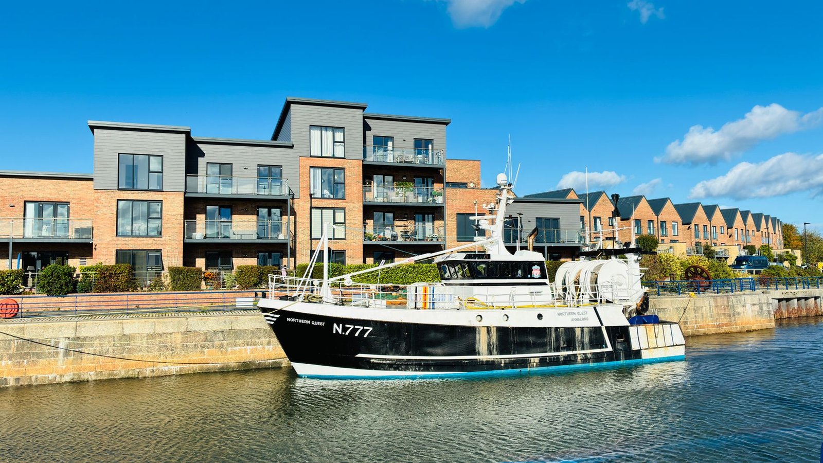 A fishing boat docked near modern apartments in Sunderland marina on a bright day.