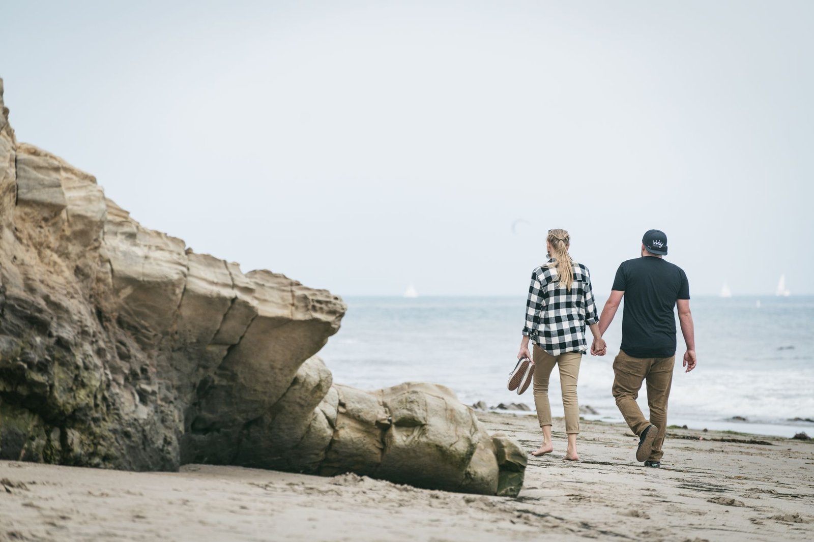 A couple holding hands and walking along a coastal beach in Santa Barbara, CA.
