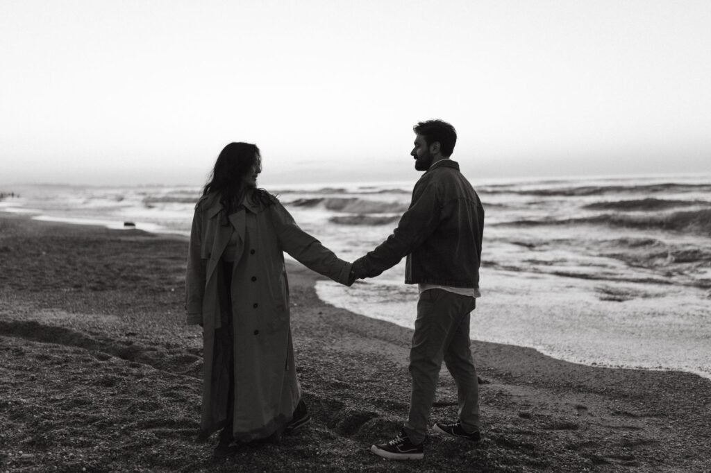 A couple holds hands on a serene beach at twilight, capturing a moment of connection.