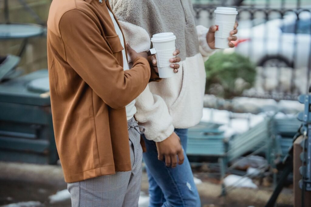 Side view of unrecognizable African American homosexual men with takeaway hot beverages strolling on street during date on bl