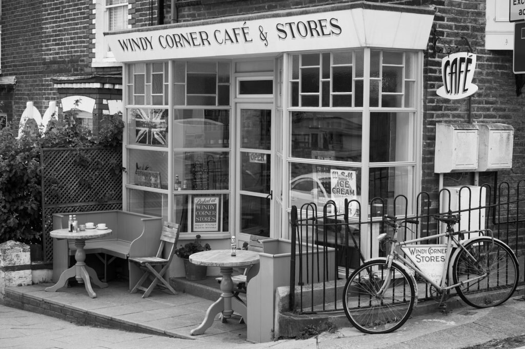 Charming black and white image of a vintage cafe facade with a classic bicycle and outdoor seating.