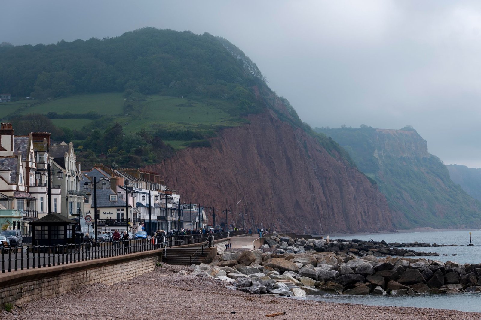 Picturesque view of the cliffs and seaside promenade in Sidmouth, UK, with misty hills in the background.