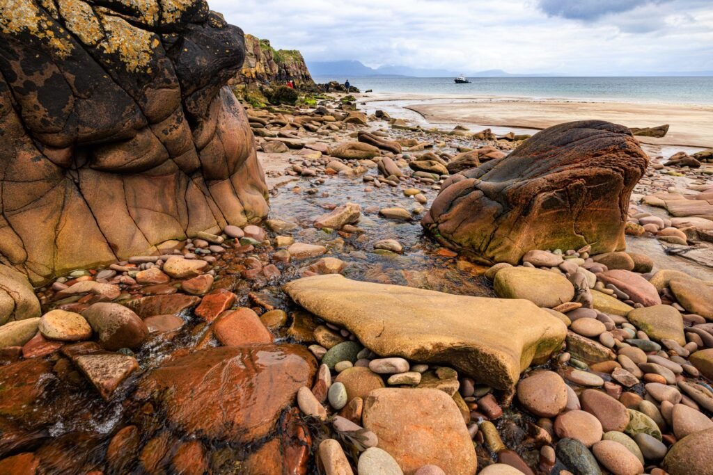 Explore the rugged beauty of a rocky beach in Scotland, featuring vibrant stones and a gentle stream.
