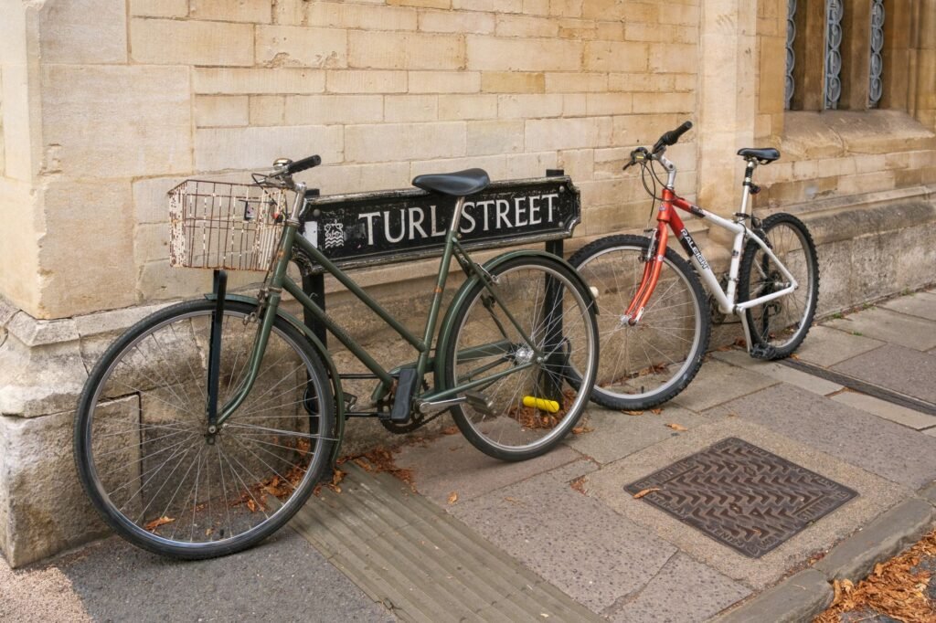 Two bicycles resting against the Turl Street sign on a historic city sidewalk.