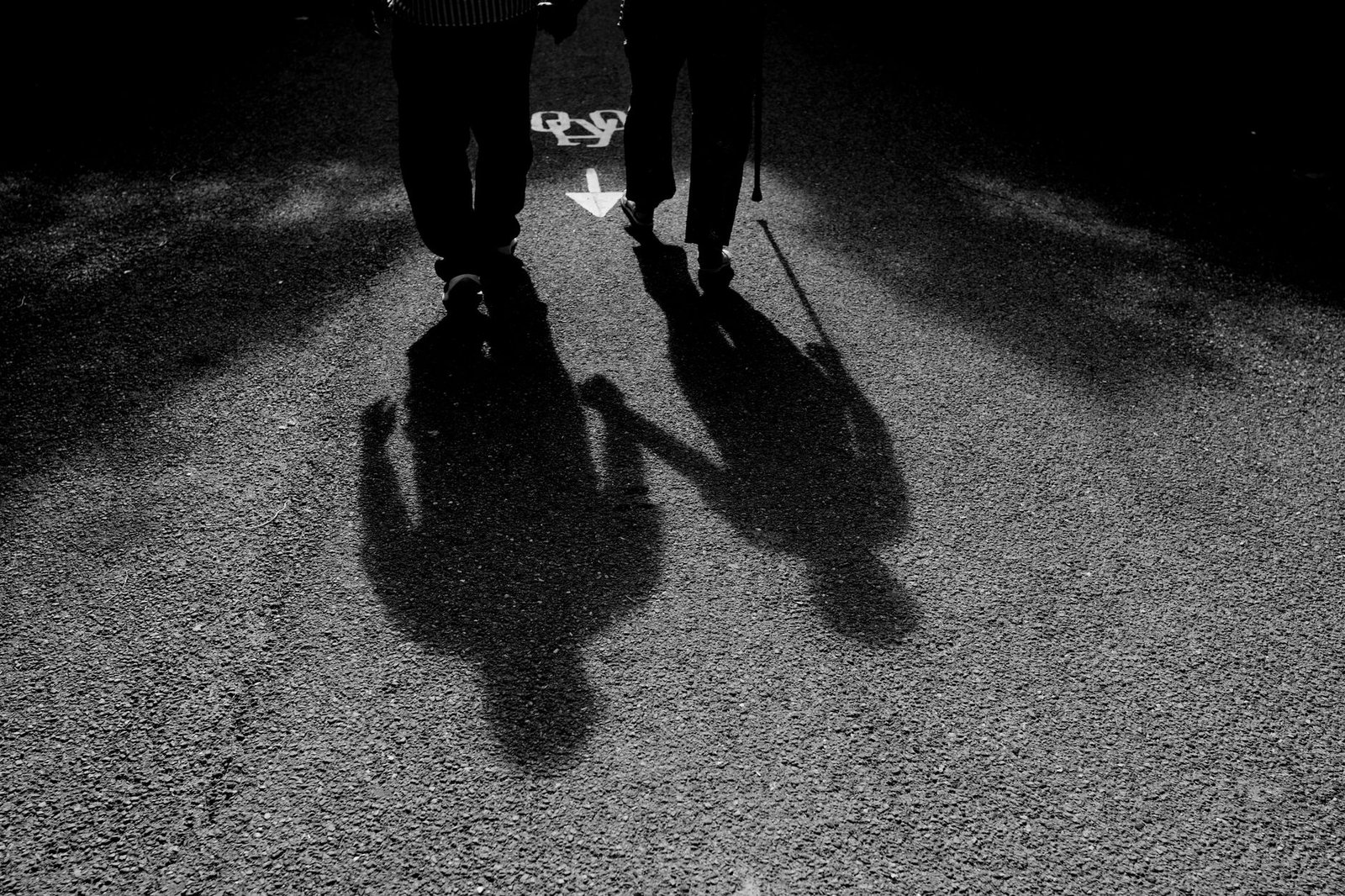 Black and white image of two people's shadows walking on a sunlit road.