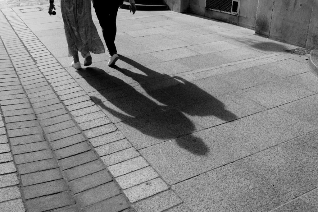 Two people walking on a street casting long shadows, in black and white.