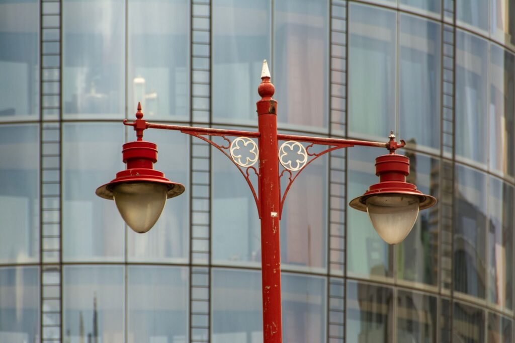 A vintage red street lamp stands before a modern glass building facade, contrasting classic and contemporary design.
