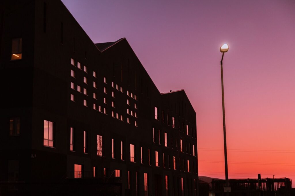 Silhouette of modern building against a vibrant sunset sky with street light.
