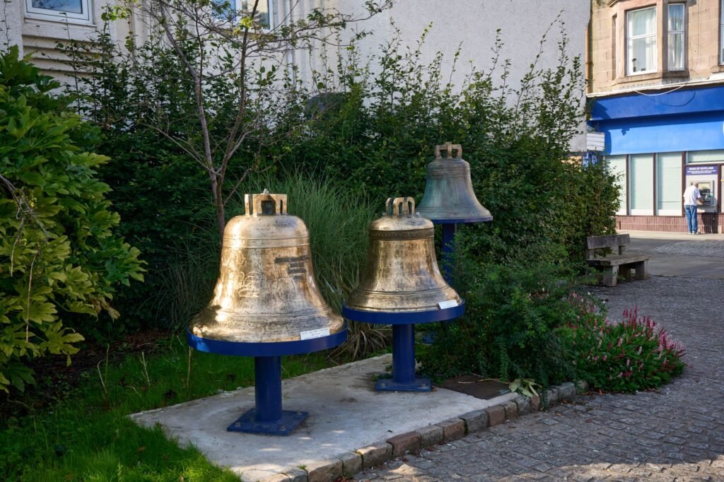 Charming historic bells displayed in a tranquil courtyard in Rothesay, Scotland during summer.