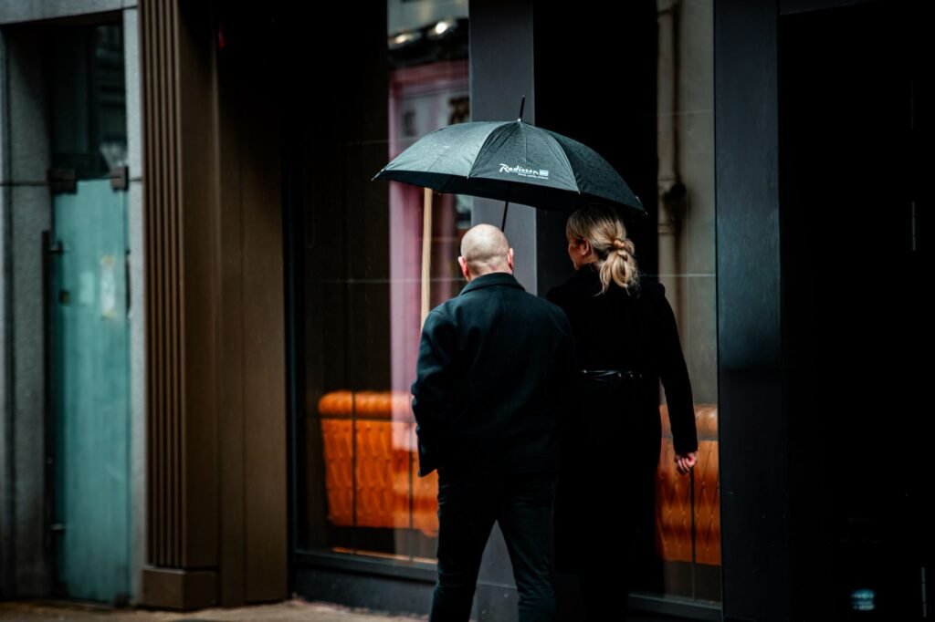 A couple walking down a rainy urban street in Ireland under a black umbrella, showcasing modern city life.