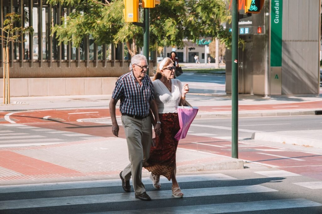 An elderly couple walking across an urban street in sunny Málaga, showcasing city life and companionship.