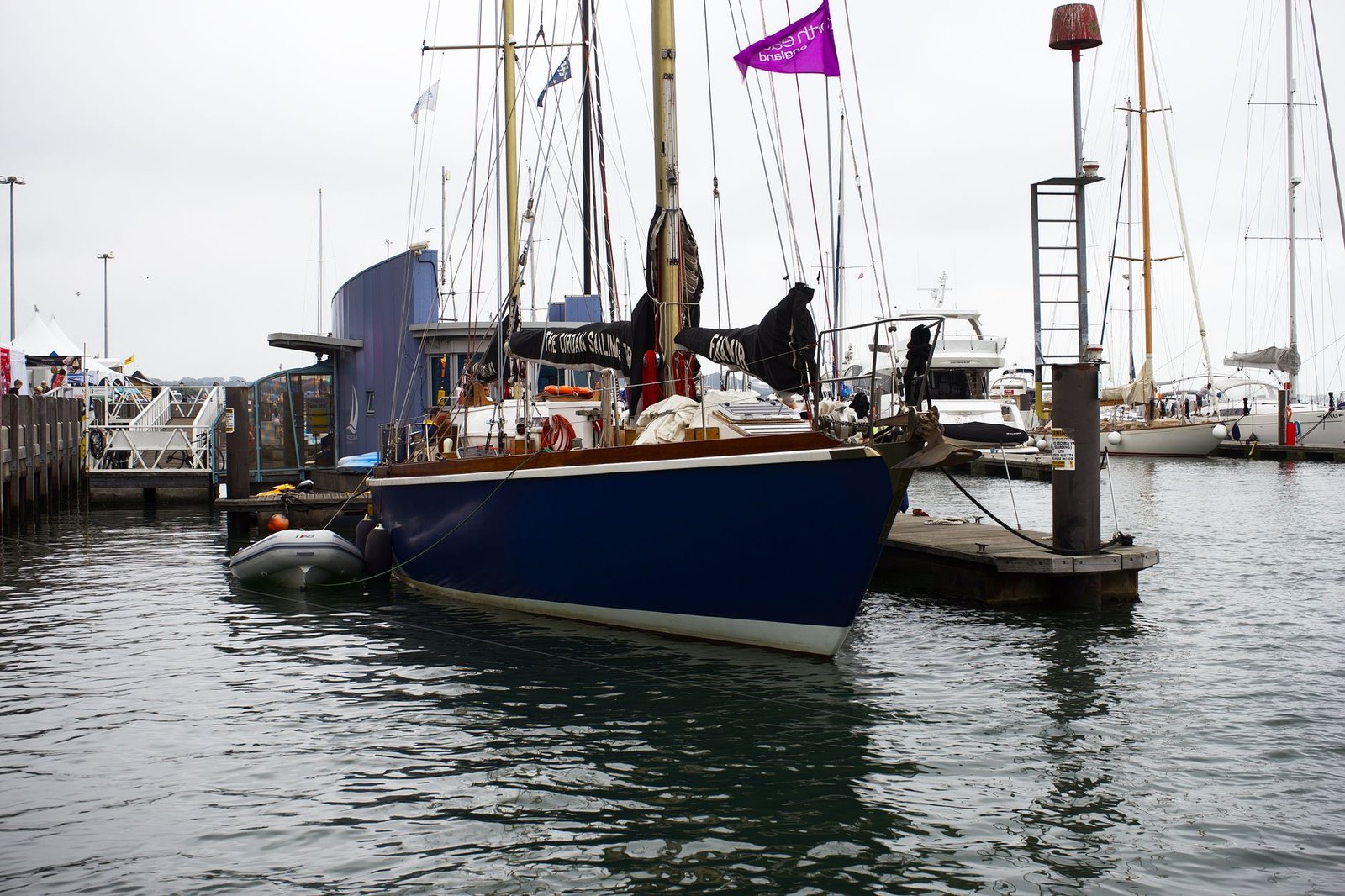 A classic blue sailboat moored at Poole Marina with surrounding yachts.