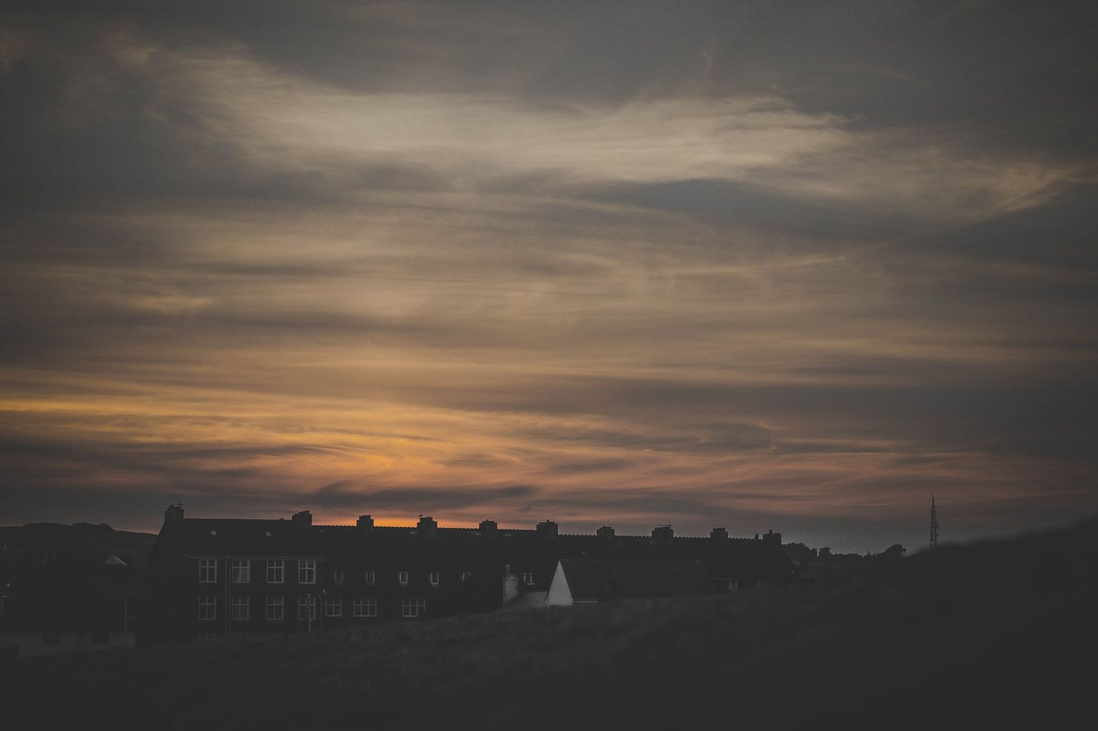 A stunning sunset over silhouetted buildings at West Bay, England with dramatic sky.