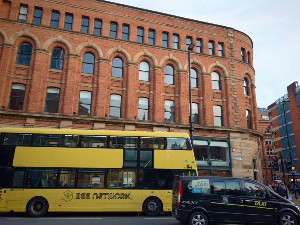 City street scene with yellow bus and taxi in front of historic brick building.