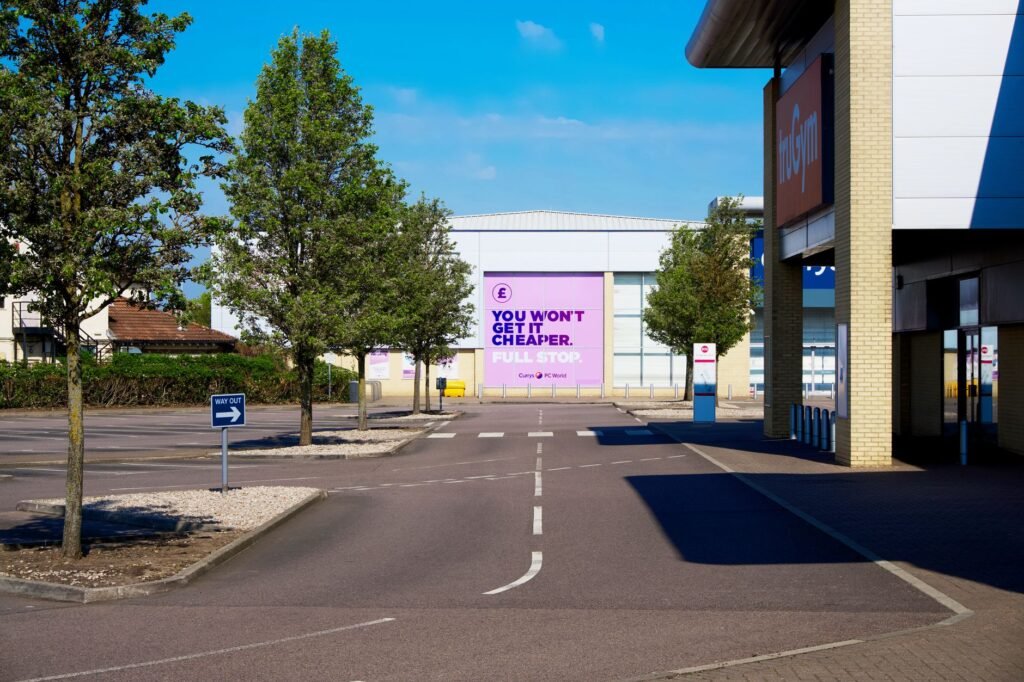 A deserted retail park with clear sky, highlighting empty spaces and trees.
