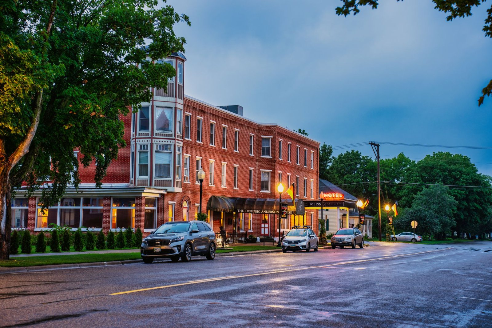 A vibrant view of a historic hotel at dusk in Wabasha, MN, with parked cars and streetlights.