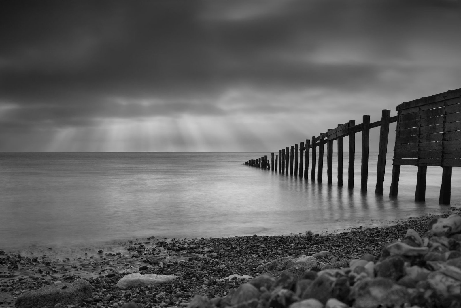Monochromatic view of a serene coastline and pier under soft light rays.