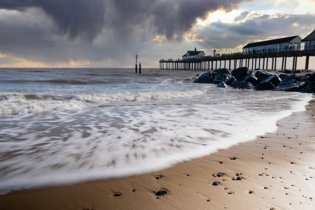 A stunning view of Southwold Pier with dramatic clouds and gentle waves on a sandy beach.