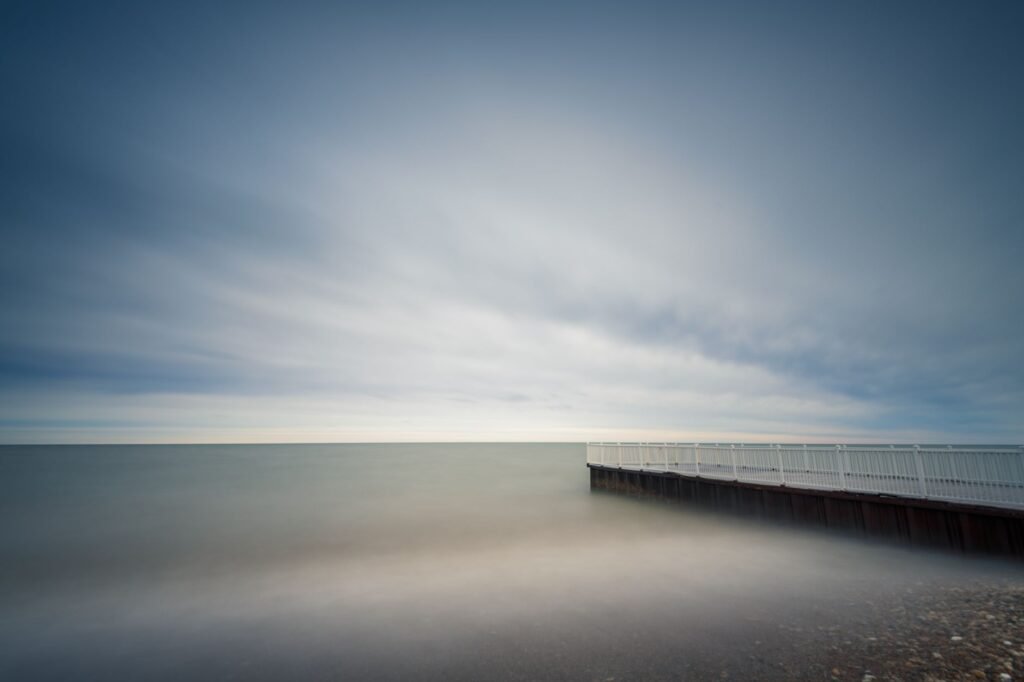 Empty pier washed by calm water of endless sea under cloudy blue sky