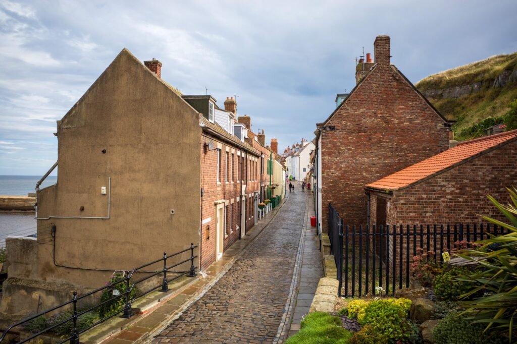 Explore the quaint cobblestone streets of Whitby, England, lined with historic brick houses and coastal views.