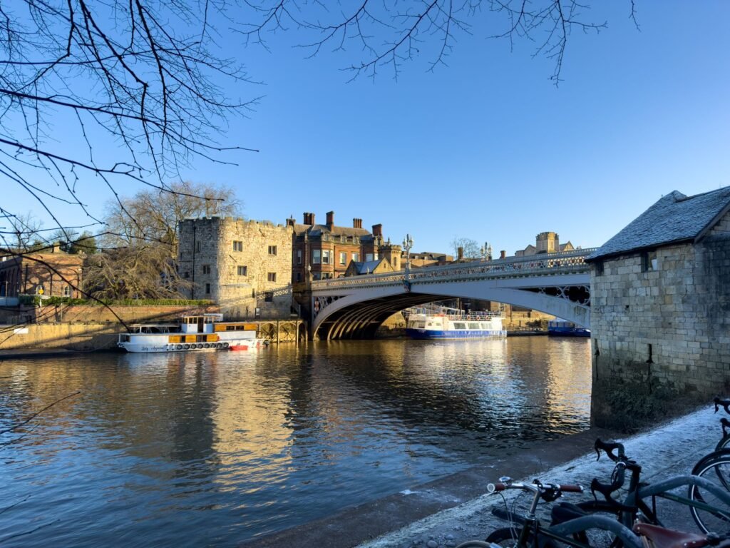 A serene winter morning view of boats by a historic bridge reflecting in the calm river.