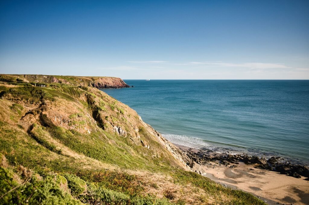 Scenic coastal cliff overlooking the ocean in Wales with clear blue skies.