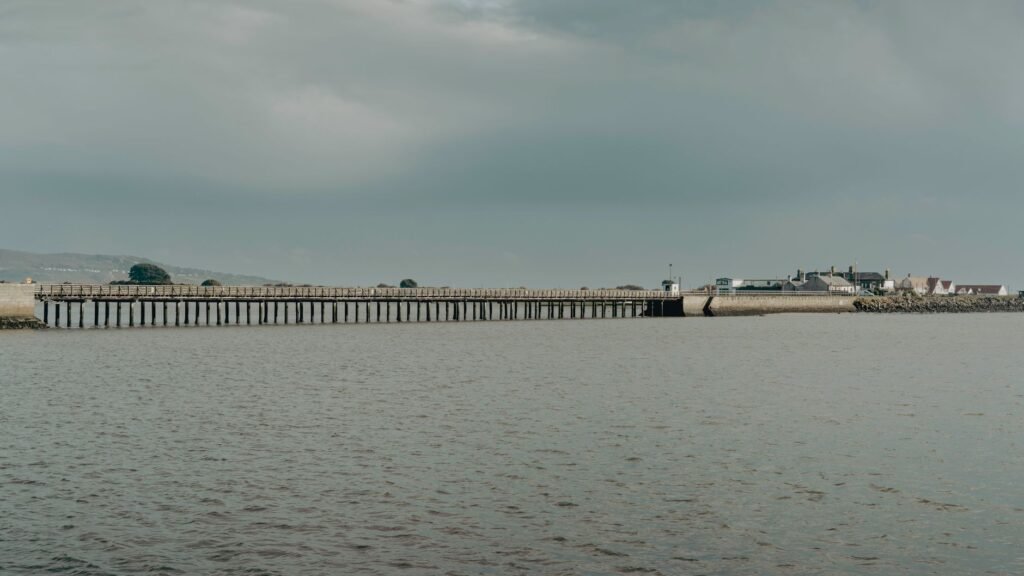 A serene landscape of a long pier stretching over the water in Ireland under a cloudy sky.
