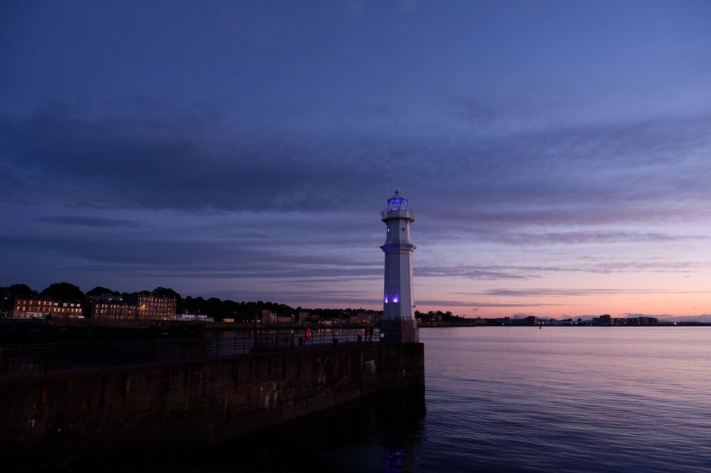 A tranquil view of Newhaven lighthouse in Edinburgh during blue hour with a calming sea backdrop.