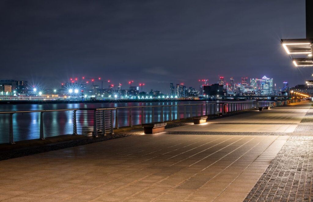 Illuminated skyline of London at night, featuring modern architecture and a tranquil promenade.