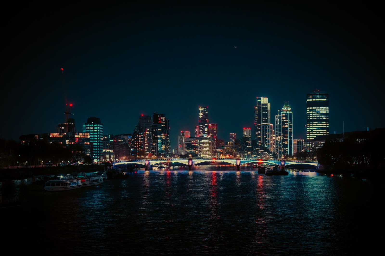 A vibrant night view of the London skyline featuring neon lights reflecting on the Thames River.