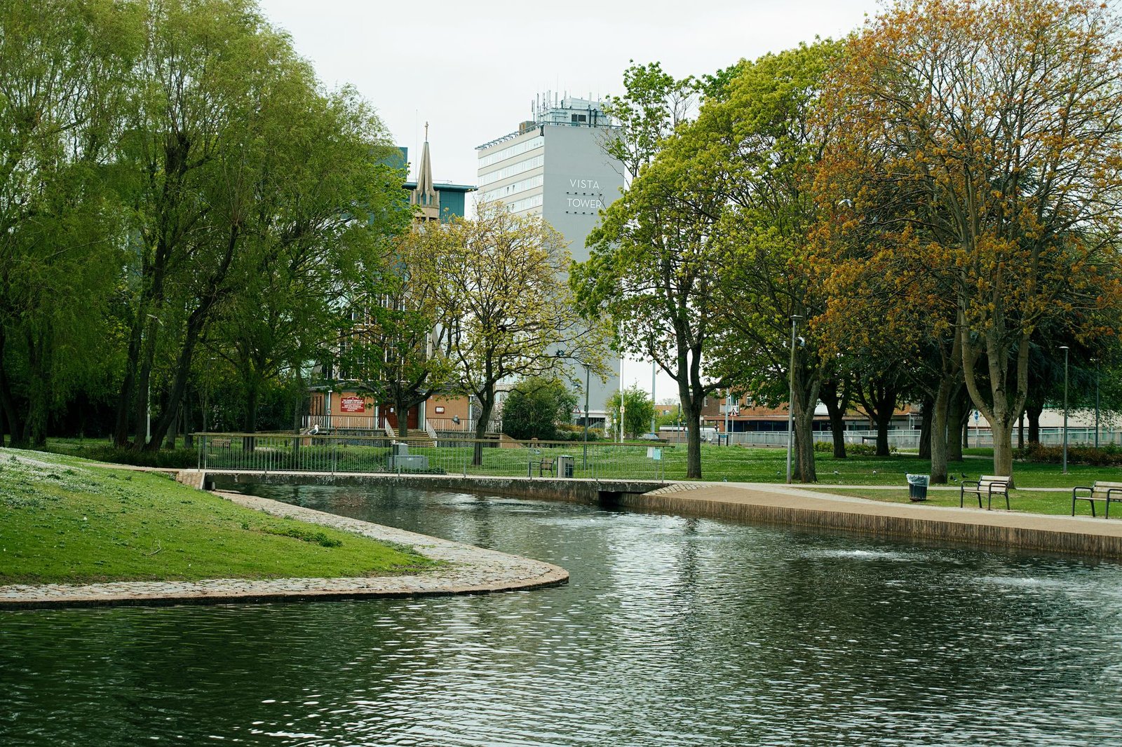 Peaceful park setting in Luton with the Vista Tower and serene water view surrounded by trees.